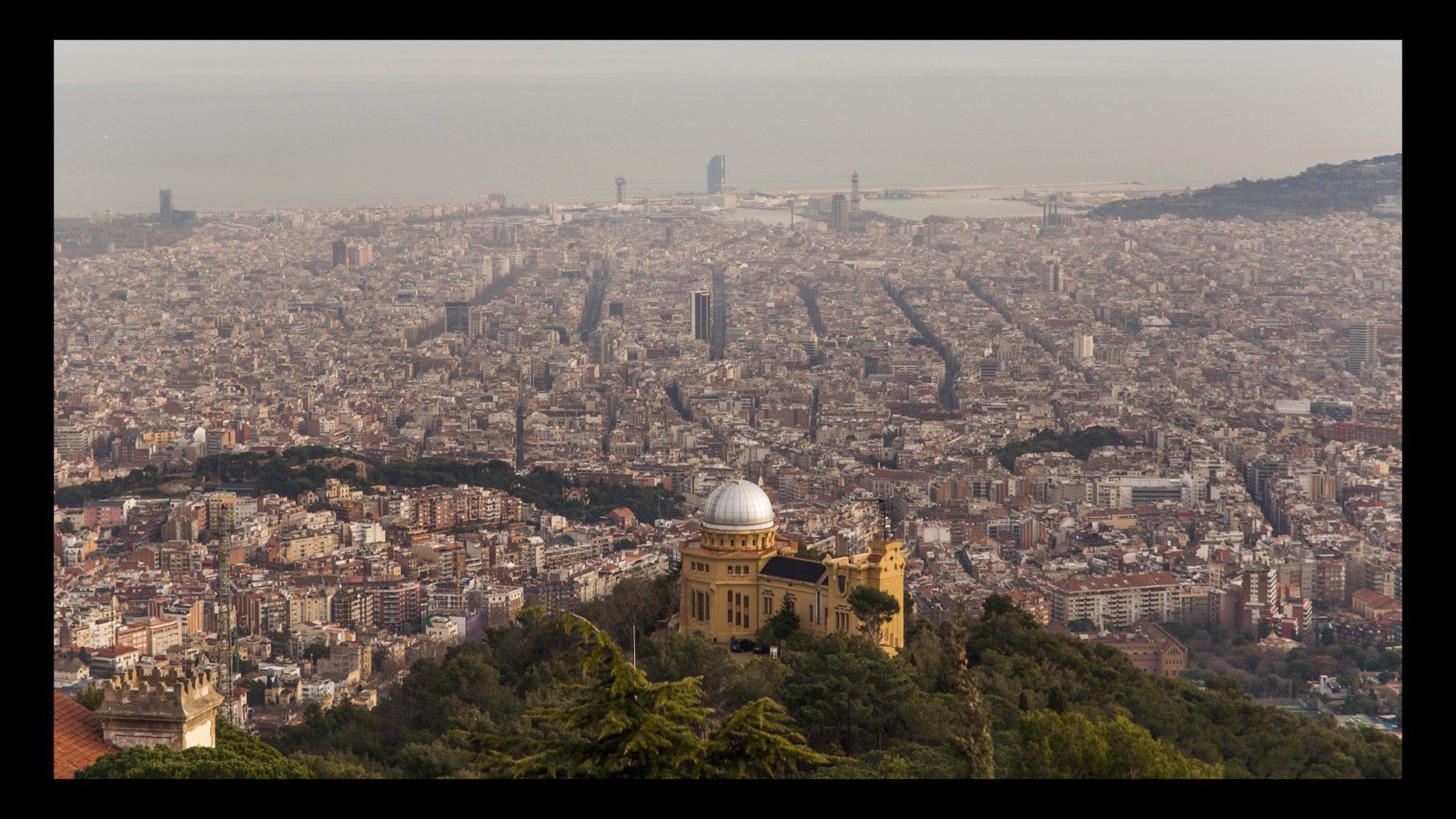 La cúpula plateada del Observatorio Fabra sobre Barcelona, con la trama de la ciudad extendiéndose hasta el puerto y el mar disolviéndose en la calima