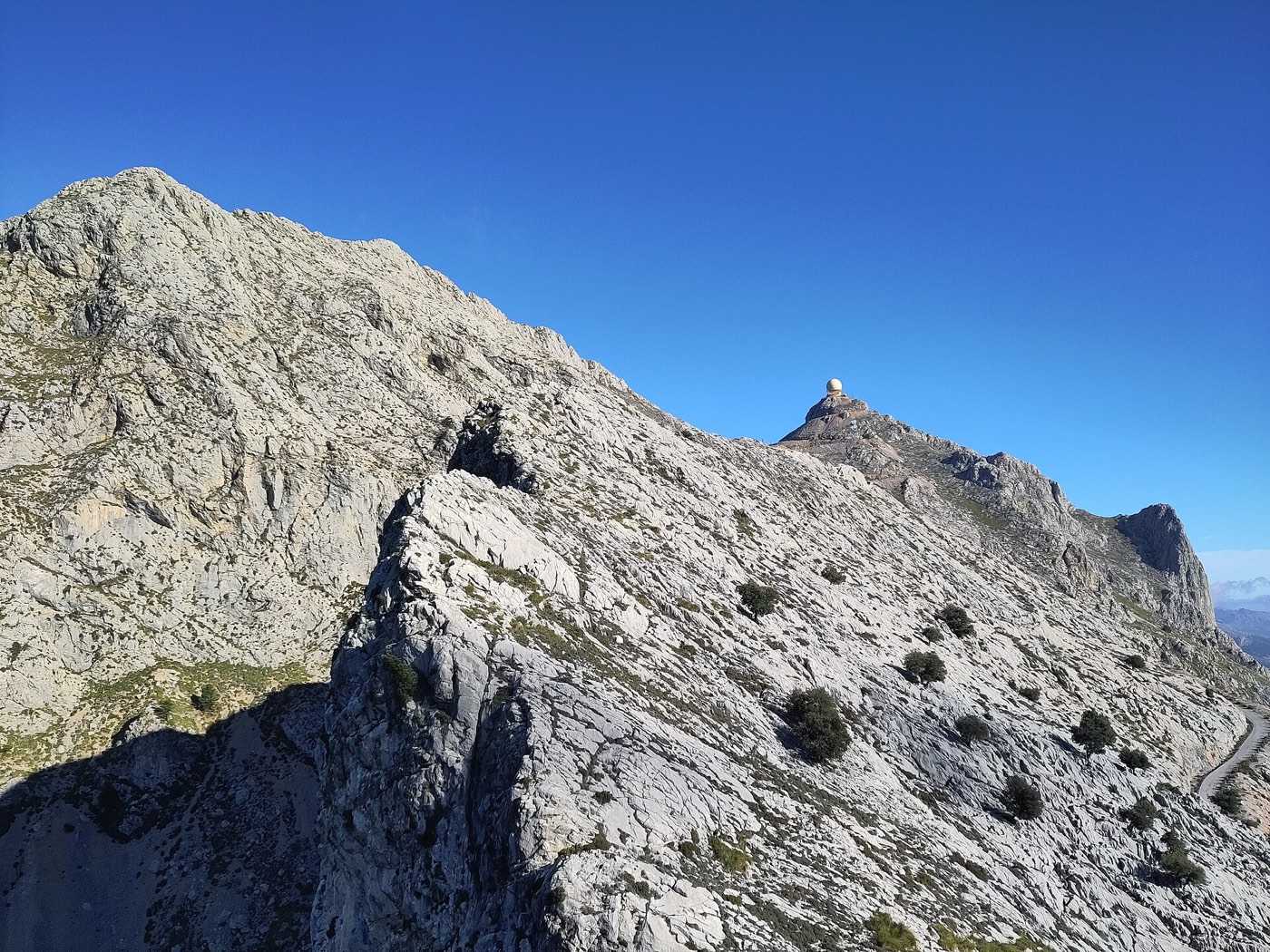 La cúpula de radar del Puig Major asomando justo por encima de una loma rocosa de la Serra de Son Torrella en primer plano
