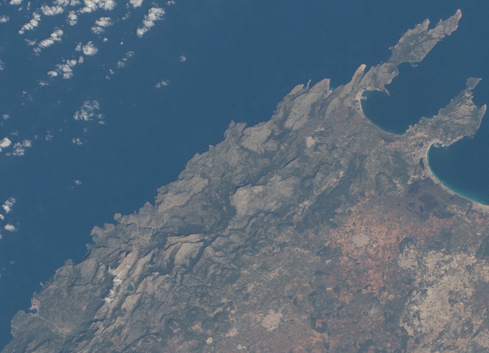 La costa noroeste de Mallorca desde la Estación Espacial Internacional: la Serra de Tramuntana como una muralla continua de roca gris a lo largo de la costa, con la península de Formentor arriba a la derecha y el interior llano de la isla detrás