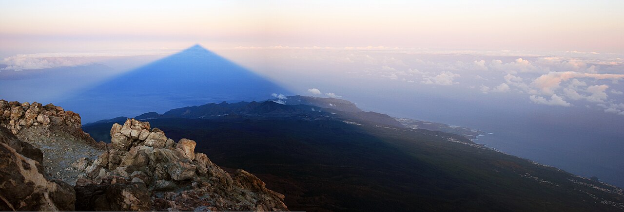 Vista panorámica desde la cumbre del Teide al amanecer con la sombra triangular extendiéndose sobre la costa de la isla y el mar