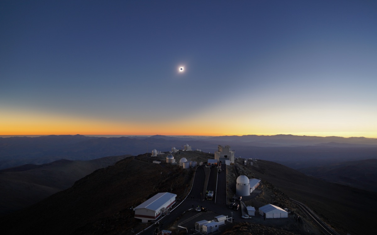 The 2019 total solar eclipse hanging low over the mountain horizon at La Silla Observatory, Chile, with sunset colours ringing the distant ridges